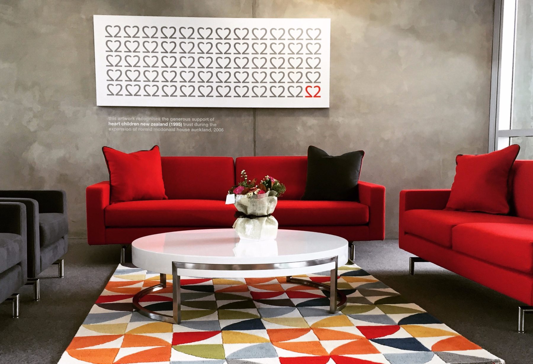 ronald mcdonald house living room setting with colourful geometric rug, red couches and concrete walls