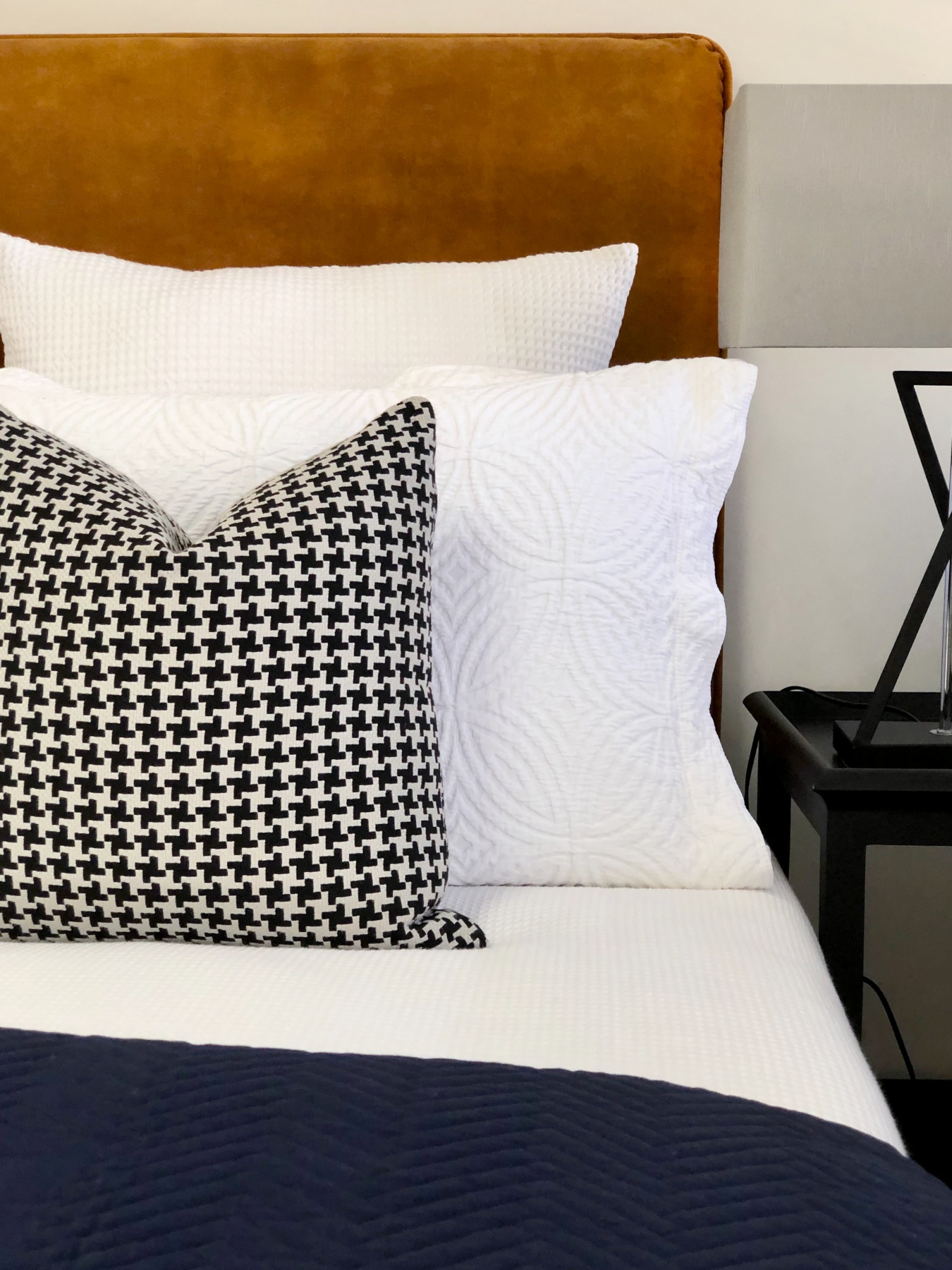 Contemporary bedroom with custom made monochrome houndstooth cushions, textured white linen, dark blue comforter and rust velvet headboard
